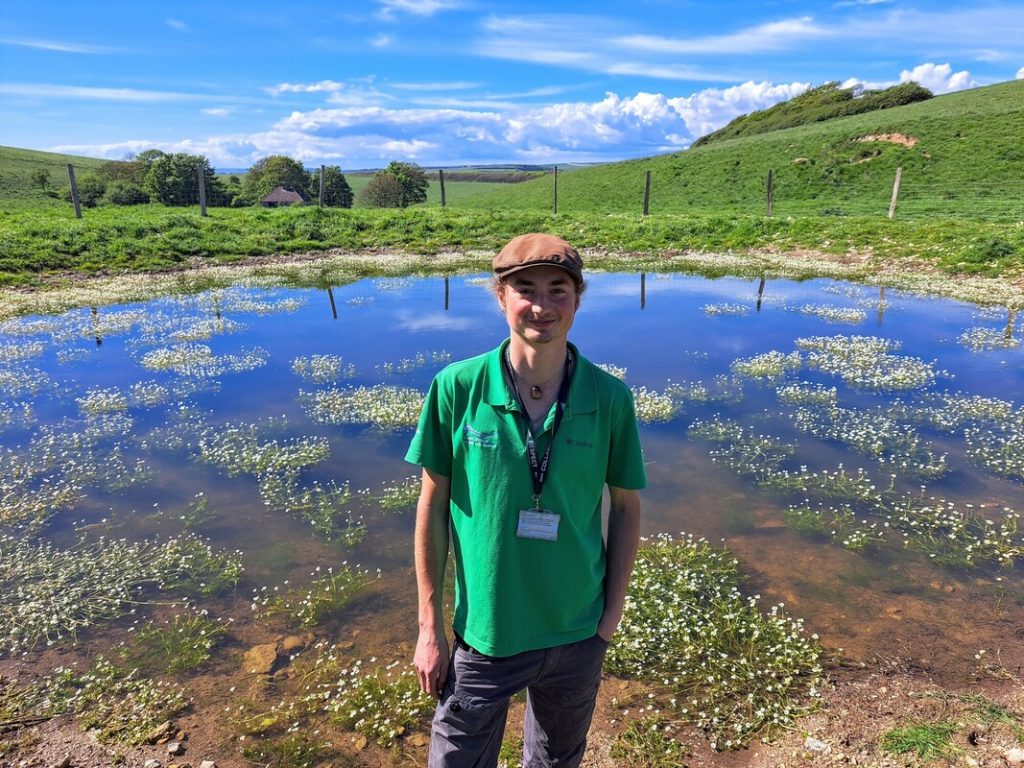 Image shows National Park Ranger Lawrence Leather next to the restored Newbarn Pond at Seven Sisters, East Sussex