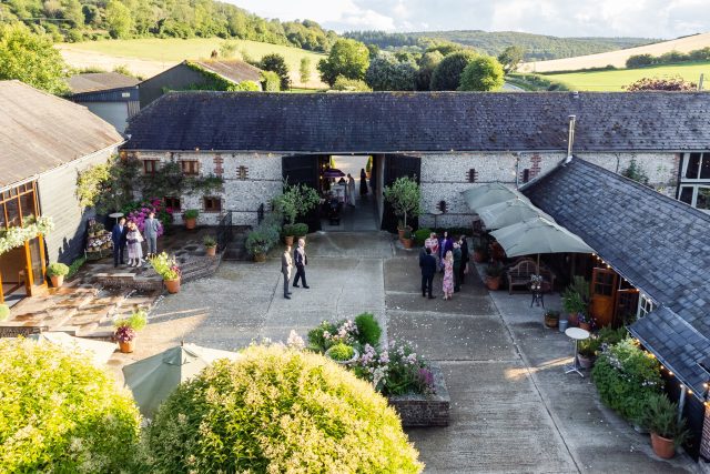 Image showing an event happening at Upwaltham Barns. A courtyard scene in a rural setting with flowers and trees surrounding.