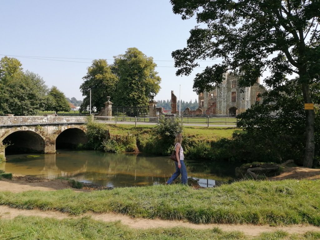 image showing the river Rother at Midhurst with the Cowdray ruins in the background and a person walking on the riverside near the bridge.