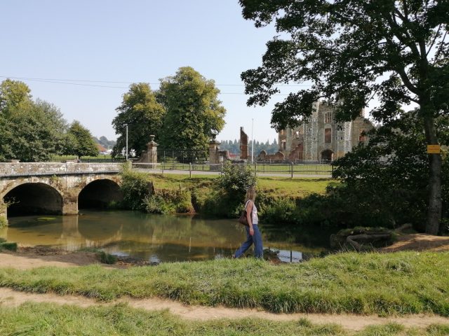image showing the river Rother at Midhurst with the Cowdray ruins in the background and a person walking on the riverside near the bridge.