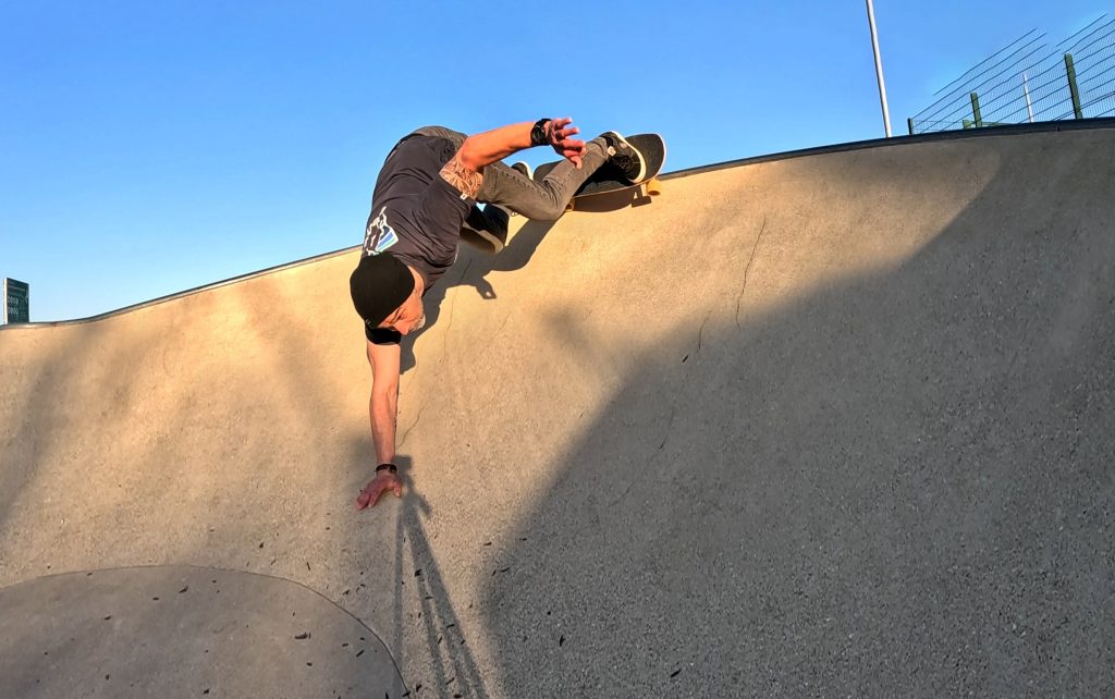 Image shows a surfskater on the turn at the top of a ridge at a skatepark.